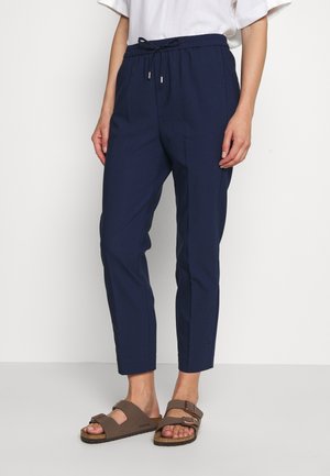 Dunkelblaue Hose mit elastischem Bund und Kordelzug, mit schmal zulaufenden Beinen und seitlichen Taschen. Getragen mit braunen Sandalen.