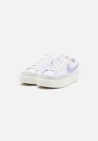 White sneakers with lavender accents, suede toe cap, and textured sides. Laces in a light shade complement the minimalist design.