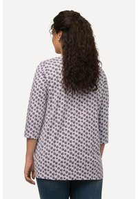 Top de color púrpura claro con mangas tres cuartos, que presenta un patrón circular negro repetido. Tejido suave con un corte relajado.