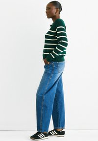 Green and white striped sweater, loose blue denim jeans, and black sneakers. Fabric is soft, with ribbed cuffs and hem. Straight-leg design.