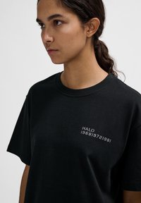 Schwarzes Baumwoll-T-Shirt mit kurzen Ärmeln, Rundhalsausschnitt und weißem Textdesign "HALO 196819721981" auf der linken Brustseite.