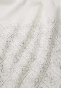 Tessuto bianco con motivo a diamante argentato e dettagli in rilievo. Il design presenta piccoli elementi scintillanti che creano una lucentezza sottile.