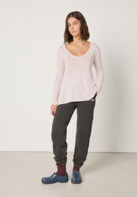 Svijetlo ružičasta majica s dugim rukavima i V-izrezom, sive trenirka hlače s rebrastim manžetama te plave klompe. Jednostavan dizajn i ležerni kroj.