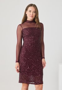 Abito di paillettes bordeaux con una silhouette aderente, maniche lunghe trasparenti e scollatura a girocollo, caratterizzato da una superficie testurizzata e un'elegante lucentezza.