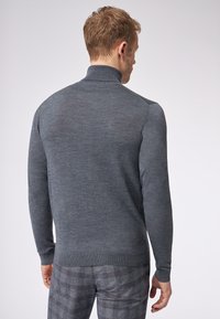 Grijze gebreide trui met hoge kraag, met een zachte textuur en aansluitend ontwerp. Draag met geruite broek, gezien vanaf de achterkant.