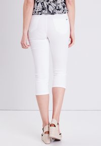 Witte capri pants met een slim-fit ontwerp, zachte textuur en twee achterzakken. Het model draagt beige plateau-sandalen.