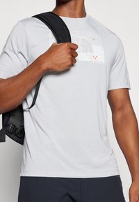 Ljusgrå kortärmad t-shirt med en grafisk design i vitt och orange, rund hals och slät textur.