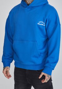 Felpa con cappuccio blu realizzata in tessuto morbido; presenta una tasca frontale e polsini a costine. Logo bianco stampato sul petto.