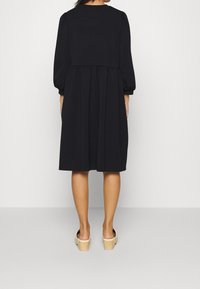 Black dress with long puff sleeves, a fitted bodice, and a pleated skirt. Made of soft fabric with a smooth texture, ends at mid-calf.