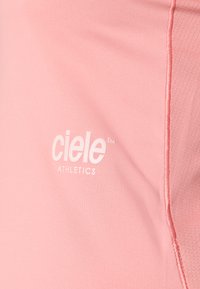 Roza atletska majica s glatkom teksturom i vidljivim bijelim logotipom s natpisom "ciele ATHLETICS" na prednjoj strani. Minimalistički dizajn.