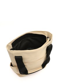 Borsa tote beige con un morbido esterno sintetico, manici in tessuto nero, chiusura con zip e una tasca interna. Presenta una texture liscia e una forma strutturata.