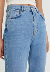 Jean en denim bleu clair à taille haute, doté de cinq poches, de coutures contrastantes et d'une coupe droite. Texture lisse.