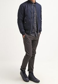 Veste bomber marine avec fermeture éclair, manches longues et poches latérales, associée à un pantalon gris foncé et des baskets montantes noires.