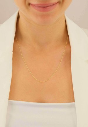 Une délicate chaîne en or repose sur une clavicule nue, avec un design fin et lisse offrant un éclat subtil.