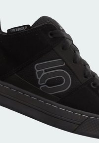 Zapatillas negras que combinan materiales de ante y malla, con punta redondeada, suela plana y acentos de logotipo reflectante.