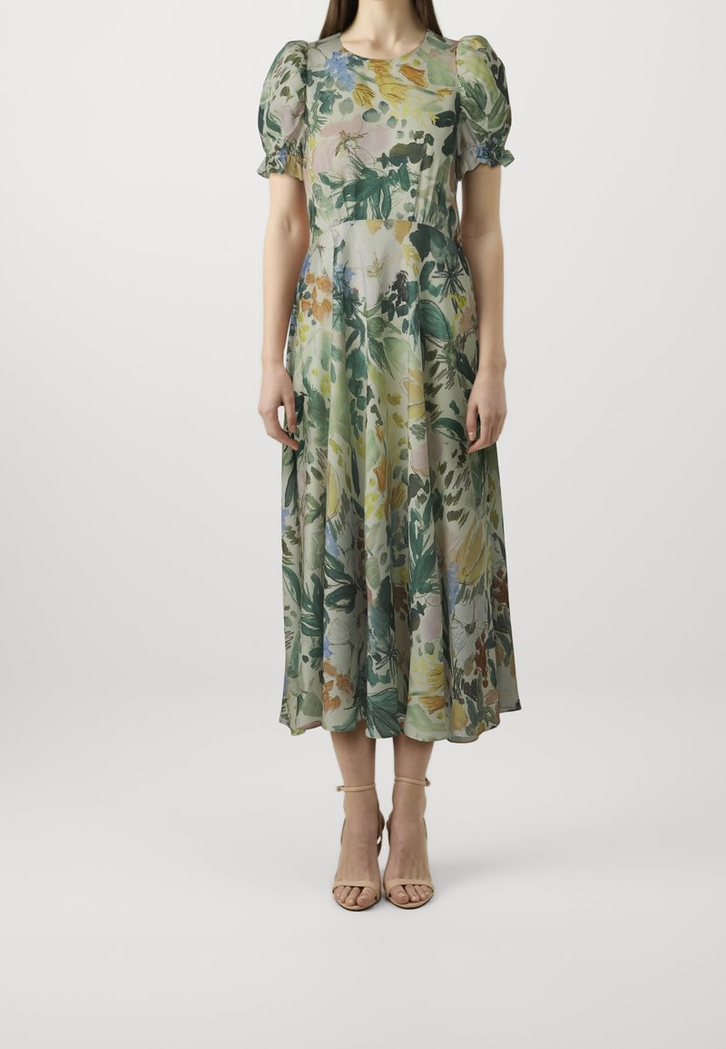 Robe midi fleurie en tissu léger, avec motifs verts, jaunes et roses, manches bouffantes et taille cintrée. Associée à des sandales nude.
