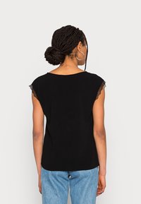 Haut noir à manches courtes avec des accents en dentelle aux épaules, à encolure ronde et coupe décontractée. Associé à un jean taille haute bleu clair.