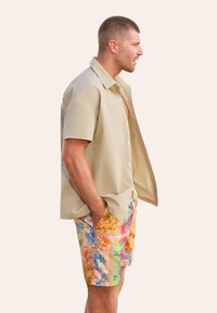 Korte mouw beige overhemd met een knopenfront, gecombineerd met levendige, patroonschorten met bloemmotieven en geometrische ontwerpen in meerdere kleuren.