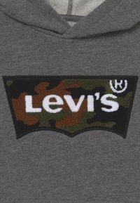 Grå hoodie med en svart lapp med ett kamouflagemönster och vit "Levi's"-text. Texturen är mjuk, med en klassisk atletisk passform och huva.
