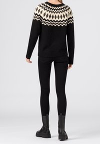 Svart tröja med ett vitt och grått geometriskt mönster på oket, med långa ärmar och en avslappnad passform. Körs ihop med svarta skinny jeans och stövlar.