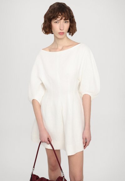 Lina kleita off-white krāsā ar laivu griezuma apkakli, pūšamām piedurknēm un paplatinātu siluetu. Modelis tur burgundijas krāsas rokassomu.