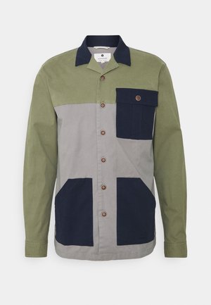 Geknoopte jas met groene, grijze en marineblauwe kleurblokken. Gemaakt van stevig materiaal, heeft het een borstzak en twee zijzakken. Bruine knopen.