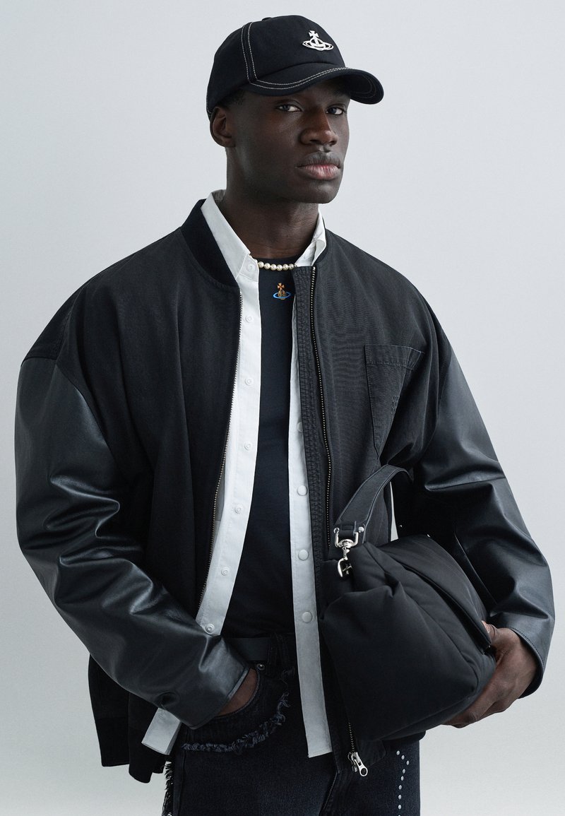 Black bomber jacket with leather sleeves, layered over a white shirt and black t-shirt. Black cap, pearl necklace, and black bag included.