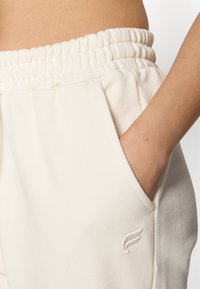 Kremasti, cotton blend trenirke s elastičnim pojasom, bočnim dzepovima i malim izvezenim logotipom na levom dzepu.