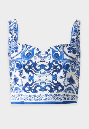Γυναίκα φορώντας λευκό και μπλε crop top με σχέδια και μακριά φούστα που ταιριάζει, στέκεται με τα χέρια στις τσέπες, φοράει λευκές γόβες.