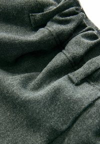Crni materijal s teksturiranim završetkom, s naboranim dijelovima i vidljivim šavovima. Mekan i fleksibilan materijal.