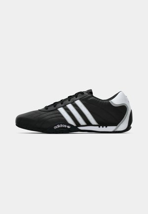 Baskets Adidas noires avec bandes blanches, accent au talon blanc et lacets noirs, montrées en profil sur fond blanc.