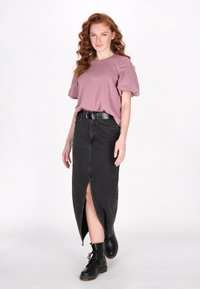 Top cu mâneci puff de culoare roz pal, fustă din denim neagră cu fanta frontală, curea neagră și ghete negre cu șireturi până la gleznă. Fondul plat accentuează contrastul.