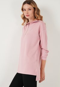 Pullover rosa chiaro con colletto a mezza zip, vestibilità rilassata, maniche a tre quarti, spacchi laterali e texture liscia. Ideale per un look informale.
