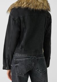 Black denim jacket with a fur collar, featuring contrast stitching, button closures, and a cropped design. Worn with high-waisted black jeans.