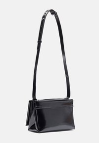 Black patent leather handbag with a structured shape, flat base, adjustable strap, and minimalistic design. Features a top zip closure.