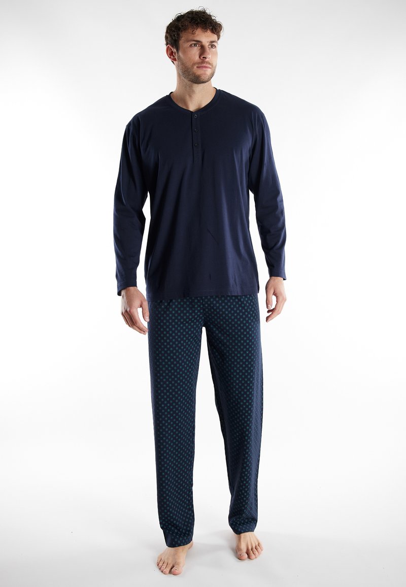Marineblaues Langarm-Henley-Oberteil mit drei Knöpfen, kombiniert mit gemusterten Schlafanzughosen, die ein wiederholtes Punktmuster in Blau und Grün aufweisen.
