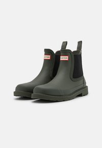 Bottes Chelsea en caoutchouc vertes avec des panneaux latéraux élastiques, un talon renforcé et une languette de logo. Elles possèdent une semelle texturée pour une meilleure traction.