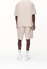 Beige t-shirt med kort ärm och matchande cargo-shorts, båda tillverkade av lättviktig tyg, med sidofickor och vita sneakers.