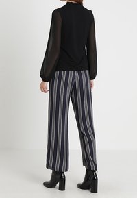 Svart topp med genomskinliga puffärmar, kombinerad med navy och vita randiga vida byxor, samt svarta klackade ankelskor.