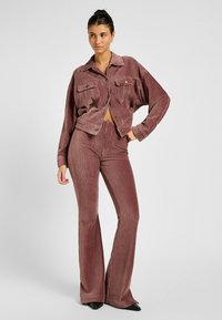 Set di giacca e pantaloni in corduroy di colore rosa polveroso. La giacca presenta tasche frontali e bottoni; i pantaloni hanno un design svasato e una texture a coste.