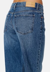 Blå denimjeans med en klassisk passform, synlig söm och en läderetikett som säger "BUBBLEROOM" på baksidan av midjan.