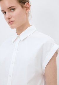 Witte kortarmige shirt met een klassieke kraag, voorzien van een knoopsluiting aan de voorkant en een zachte katoenen textuur. Simpel, schoon ontwerp.