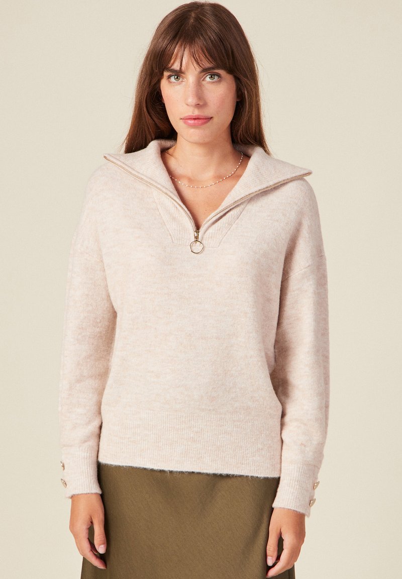 Maglione a maglia beige chiaro con collo a mezza zip, polsini a coste e un dettaglio a tre bottoni sulla manica. Texture morbida e vestibilità comoda.