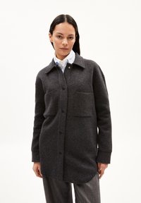 Giacca camicia in misto lana grigio scuro con chiusura a bottoni, vestibilità oversize, due tasche frontali e colletto a punta. Texture liscia, design minimalista.