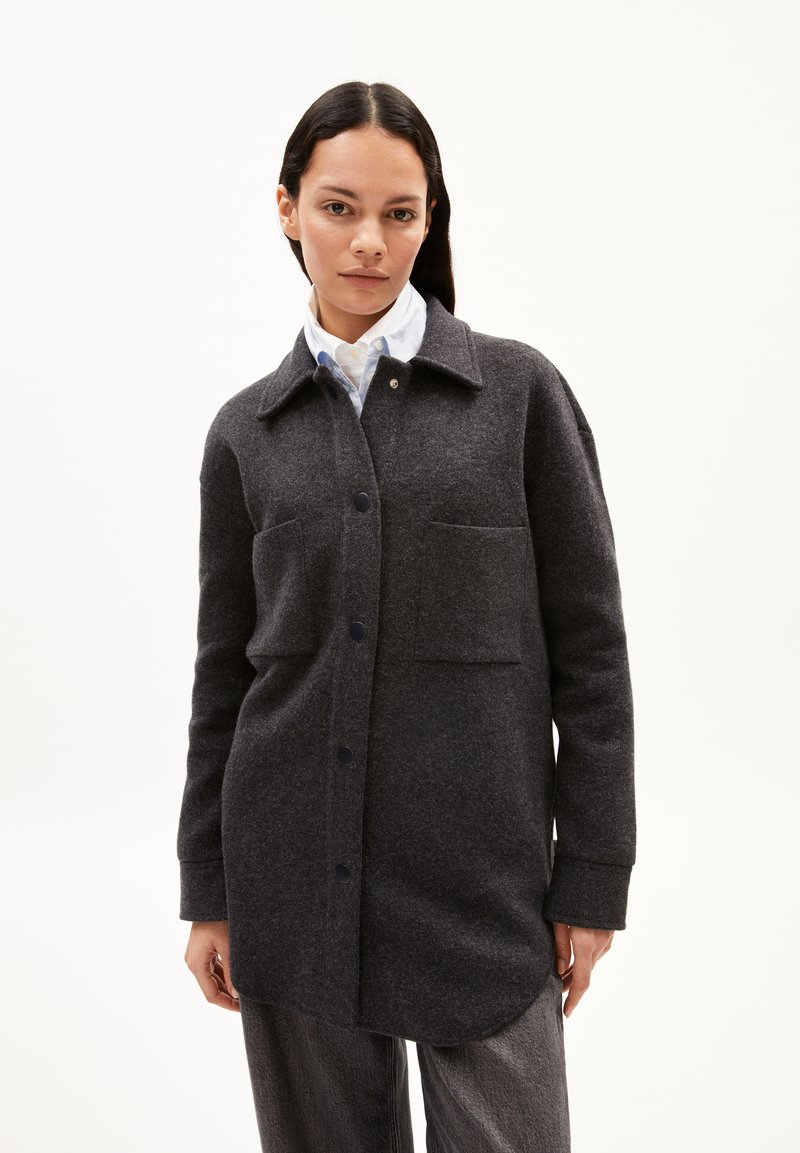 Giacca camicia in misto lana grigio scuro con chiusura a bottoni, vestibilità oversize, due tasche frontali e colletto a punta. Texture liscia, design minimalista.