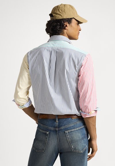 Πολύχρωμο ριγέ πουκάμισο με κίτρινες, μπλε, κόκκινες και λευκές πτυχές, με μανίκια που έχουν γυριστεί και κλασικό γιακά, συνδυασμένο με μπλε τζιν.