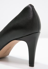 Chaussure à talons hauts noire avec une texture lisse semblable à du cuir. Présente un talon effilé et un bout arrondi, avec une légère brillance sur la surface.