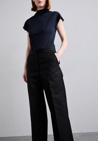 Marinblus med korta ärmar som passar bra ihop med högmidjade svarta byxor. Den släta texturen och raka klippningen ger en skräddarsydd look.