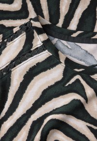 Grön och beige mönstrad tyg med zebramönster. Har en rund halsringning och texturerade detaljer längs axelsömmarna.