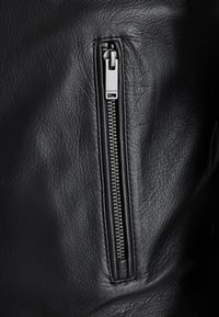 Jachetă din piele neagră, cu un buzunar cu fermoar și accesorii din metal argintiu, textură elegantă și detalii subtile de granulație pe suprafață.